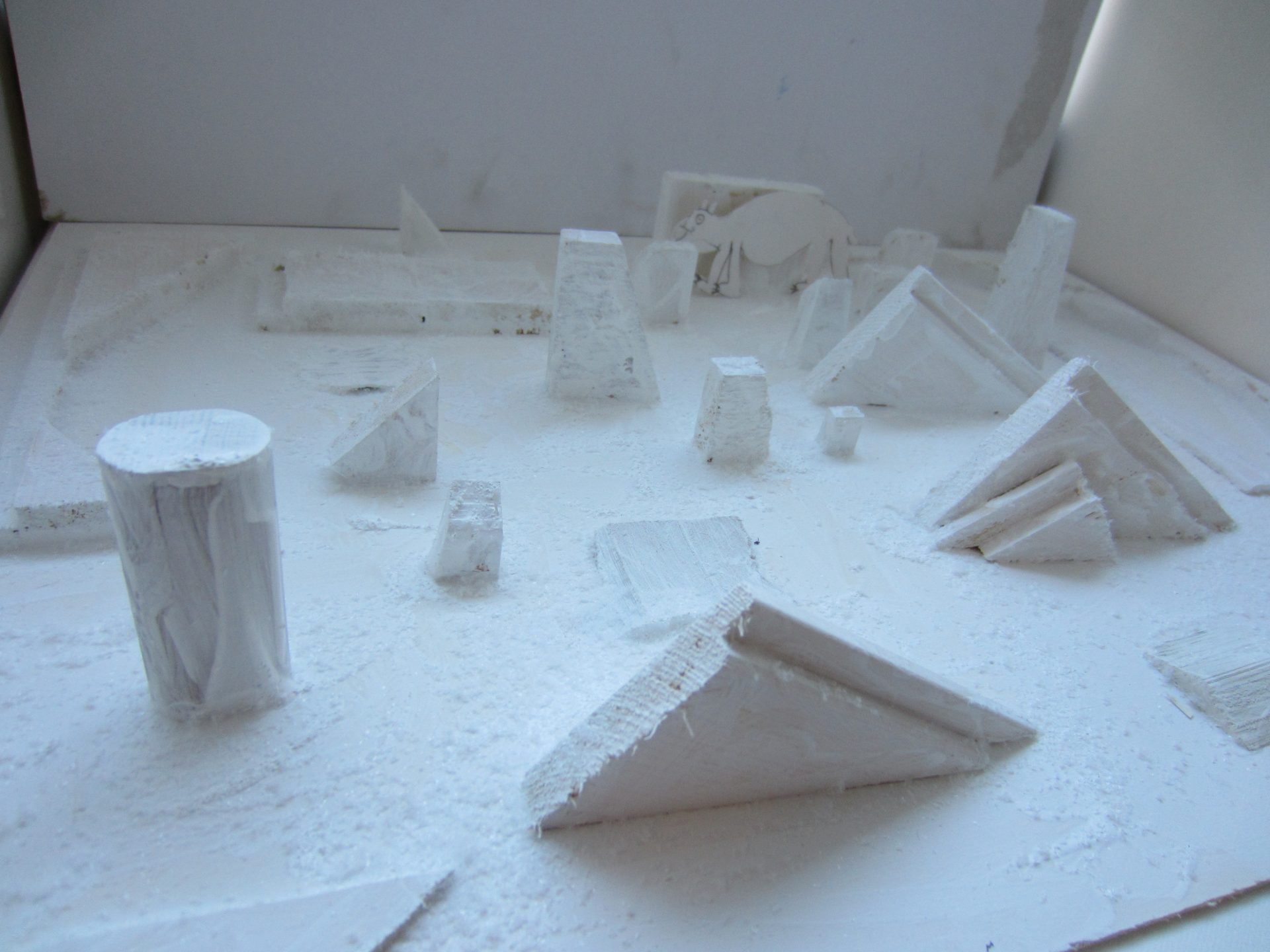 Eine Sammlung weißer geometrischer Formen, darunter Zylinder, Prismen und Pyramiden, sind auf einer flachen Oberfläche vor einem weißen Hintergrund angeordnet und bilden eine abstrakte, minimalistische Szene.