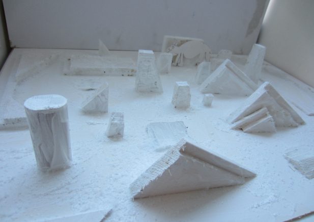 Eine Sammlung weißer geometrischer Formen, darunter Zylinder, Prismen und Pyramiden, sind auf einer flachen Oberfläche vor einem weißen Hintergrund angeordnet und bilden eine abstrakte, minimalistische Szene.