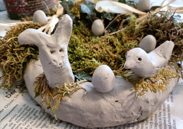 Ein handgefertigter Kranz aus Ton, verziert mit Moos, Toneiern, einem Tonhasen und einem Tonvogel, ausgestellt auf einer Zeitung.