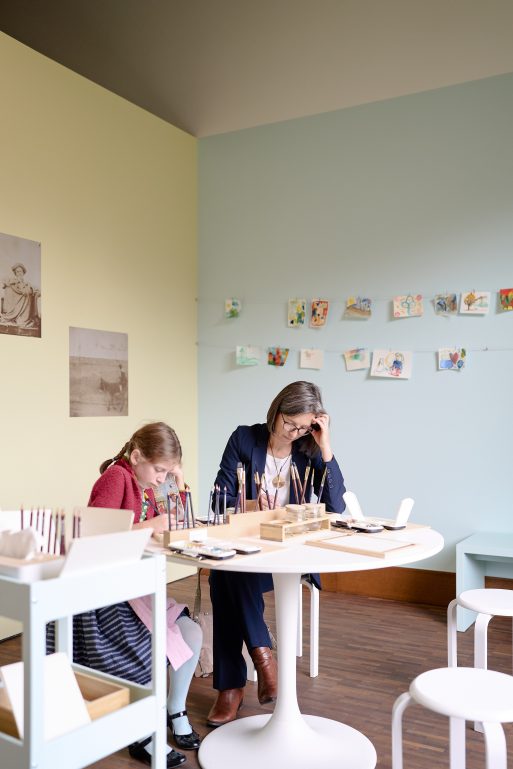 Ein junges Mädchen und eine Frau sitzen an einem runden Tisch und arbeiten beide mit Pinseln und Malutensilien an Kunstprojekten.